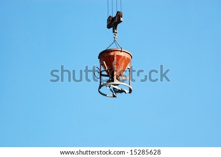 Charging hopper with concrete mix being transported by jib crane over blue sky