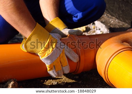 Closeup of plumber\'s hands assembling pvc sewage pipes in house foundation