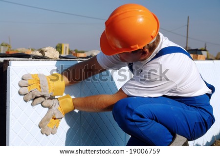 Construction worker thermally insulating house foundation walls with styrofoam boards