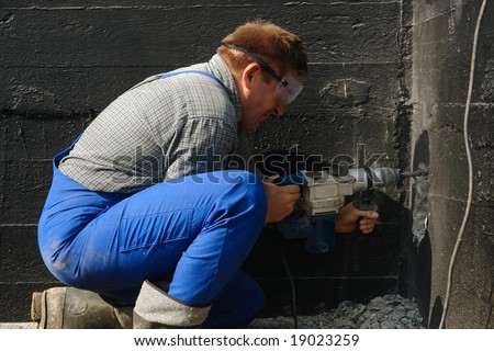 Construction worker making a culvert in foundation wall for sewage pipe using pneumatic hammer