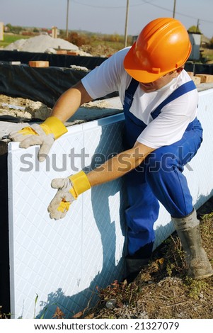 Construction worker fitting thermal insulation panels to house foundation walls