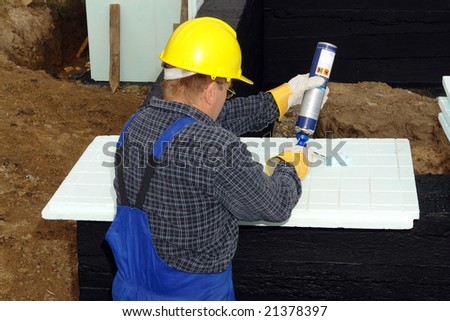 Construction worker applying glue on thermal insulation styrofoam panels to be fixed to house foundation walls