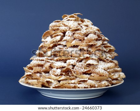 Plate full of traditional Polish sweet crispy biscuits called Faworki with caster sugar over dark blue background