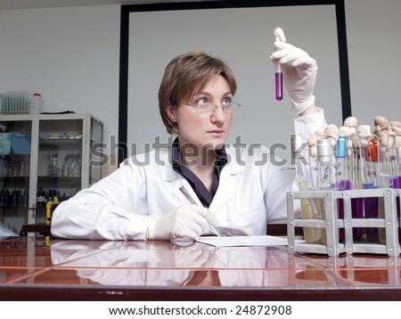 Female laboratory technician sitting behind laboratory desk looking at specimen taking observation notes