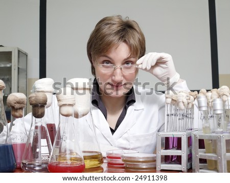Portrait of female laboratory technician sitting behind laboratory desk with flasks and test tubes
