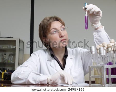 Female laboratory technician sitting behind laboratory desk looking at specimen taking observation notes