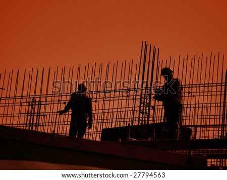 Silhouettes of construction workers working with steel reinforcement against orange sky
