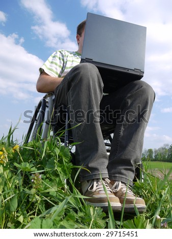 Handicapped man on wheelchair using laptop outdoors