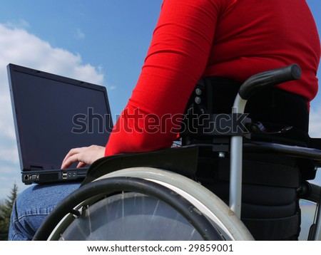 Handicapped woman on wheelchair using laptop outdoors