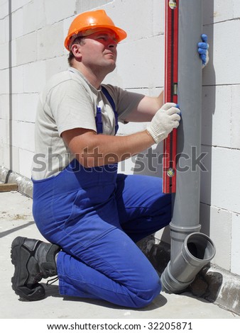 Plumber using level for checking plumb line of assembled pvc sewage pipes inside unfinished house