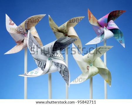 Toy windmills cut from five major world currency banknotes over blue sky