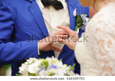 bride putting on wedding ring on groom\'s finger