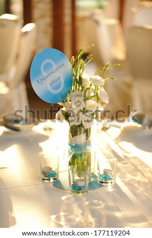 vase with flowers and table number on table in sunlight