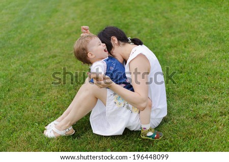 mother biting her laughing daughter on grass