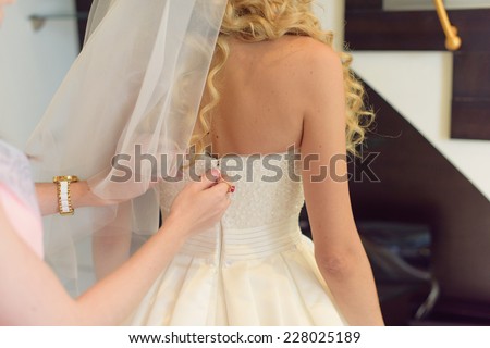 bridesmaid zipping wedding dress on bride