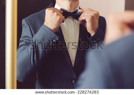 groom looking in mirror and touching bowtie