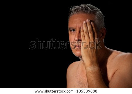 Handsome unshaven middle age man with salt and pepper hair and bare chested on a black background.