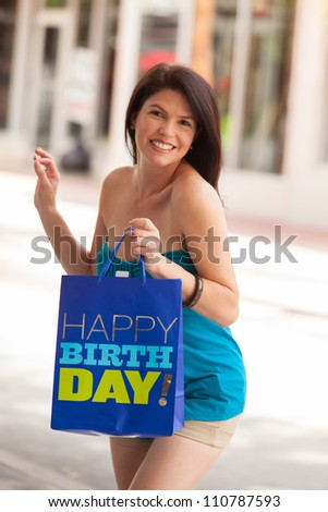 Beautiful woman outdoors in a shopping mall holding a happy birthday bag.