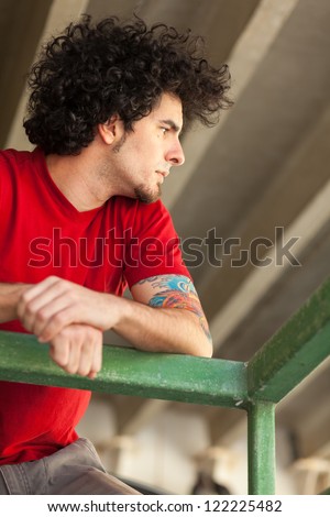 Handsome young man with long curly hair and goatee in a outdoor urban setting.
