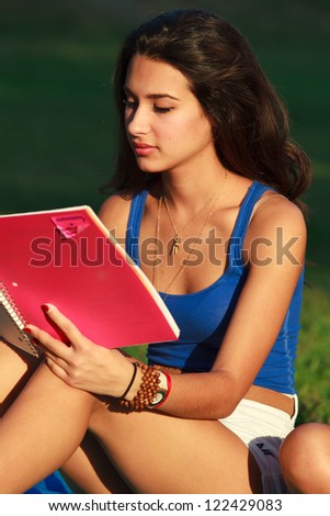 Beautiful multicultural young college woman studying outdoors on campus.