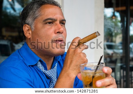Handsome middle age Hispanic man smoking a cigar with a cocktail.