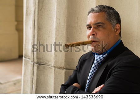 Handsome middle age Hispanic man smoking a cigar outdoors in a urban setting.