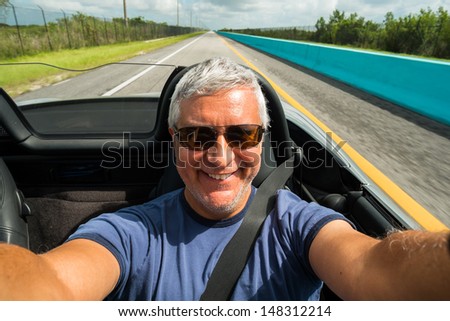 Handsome middle age man driving a convertible automobile on the highway.