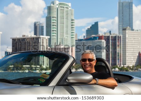 Handsome middle age man in a convertible automobile with a downtown skyline background.