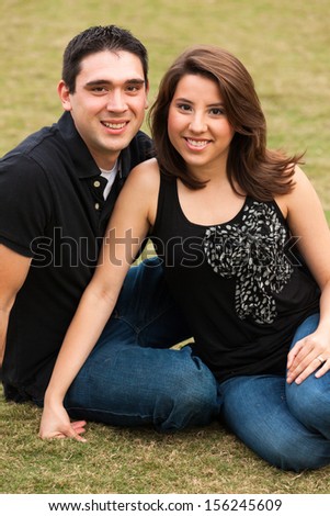 Young married couple  in a loving pose sitting on a lawn in a park.