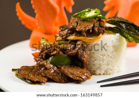 Fancy sliced Asian pepper steak served with white rice and garnished with carved carrot swans on a white plate.