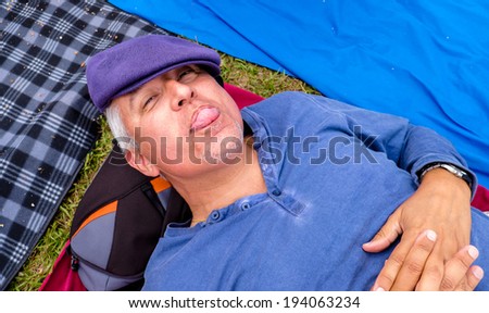 Handsome middle age man lying down outdoors with a funny expression.