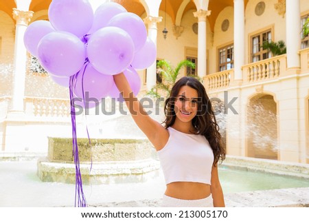 Beautiful young woman in a outdoor courtyard setting holding balloons.