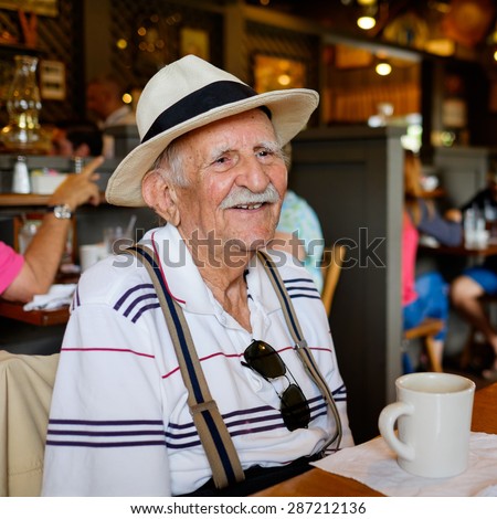 Elderly eighty plus year old man wearing a hat in a restaurant setting.