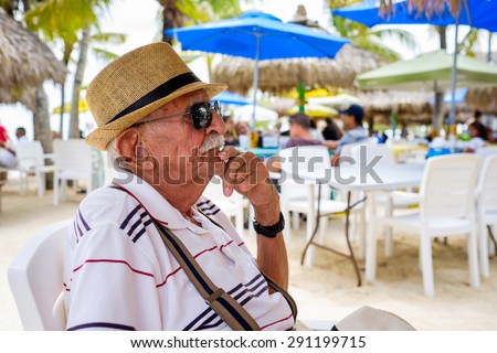 Elderly eighty plus year old man wearing a hat in a outdoor restaurant setting.