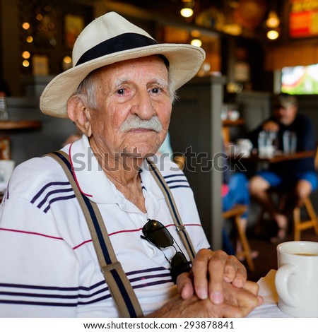 Elderly eighty plus year old man wearing a hat in a restaurant setting.
