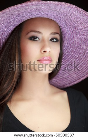 Beautiful and exotic young woman of multiple ethnicity wearing a purple hat with a black background.