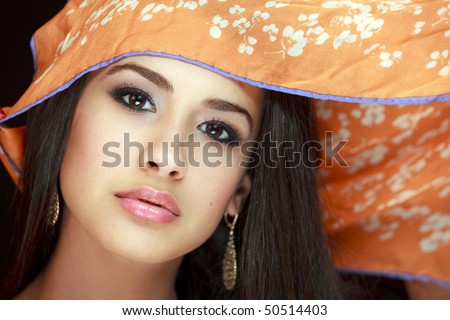 Beautiful young woman of multiple ethnicity in a glamour/fashion pose with a scarf over her head with a black background.