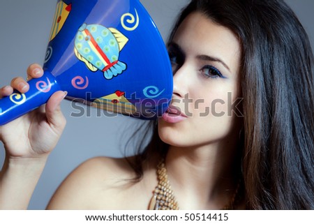 Beautiful young woman of multiple ethnicity in a glamour/fashion pose holding a large blue martini glass with a gray background.