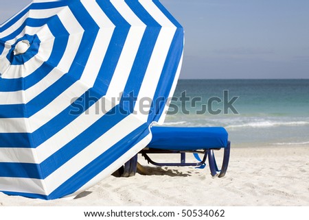 Image of blue lounge chair and blue and white striped umbrella set against the South Beach Atlantic shoreline in the late afternoon in Miami Beach.