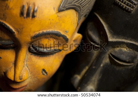 Close-up shot of a pair of wooden African tribal masks with color contrast. Macro lens was used with a shallow depth of field on the black mask to create a sense of mystery.
