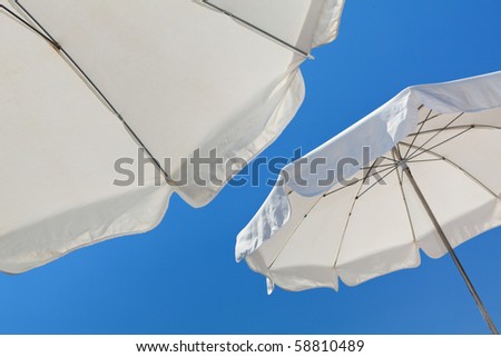 White beach umbrellas against a blue sky in the French Riviera in Nice, France.