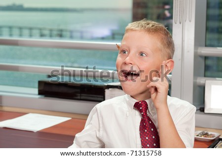 Cute young boy in business clothing in a business office with a funny expression and missing tooth.