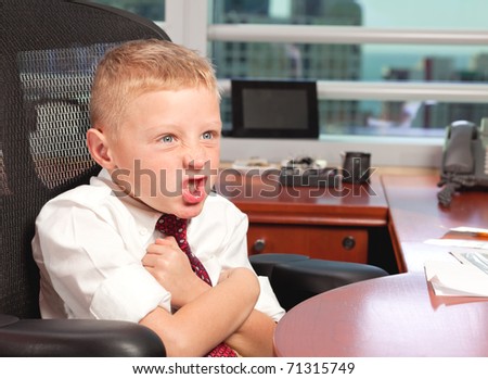 Cute young boy in business clothing in a business office with a angry expression and missing tooth.