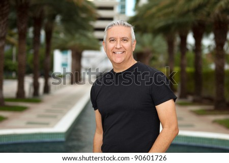 Handsome middle age man in an outdoor urban setting with a long row of palm trees in the background.