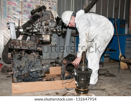 the worker in protective clothes repairs the automobile mechanism