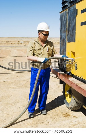The worker fills the compressor with fuel on industrial site