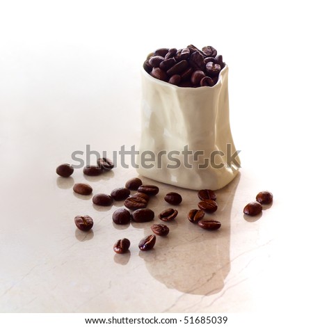 A ceramic bag filled with coffee beans spilling onto a marble surface in square format