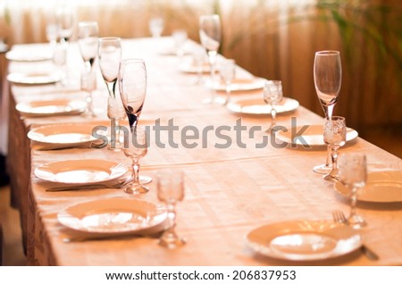 Table laid by a white cloth and with the laid-out tableware on it on the indistinct  restaurant background