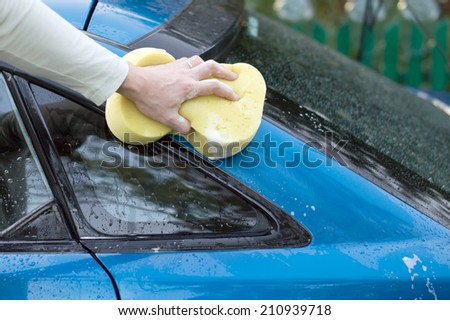 The process of washing a blue car with the help of shampoo and yellow sponges in the yard