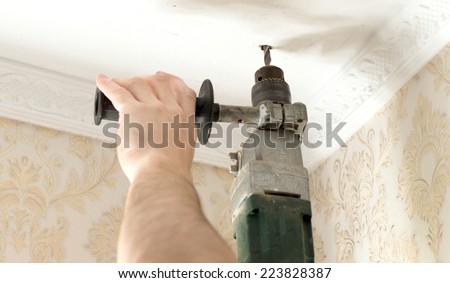 The process of drilling a white plaster ceiling with an electric drill